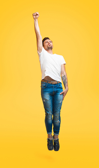 Handsome guy grimacing while jumping in superhero flying pose on bright yellow background