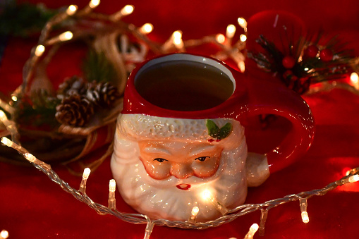 Santa Claus shaped tea mug with tea inside and Christmas lights and ornaments