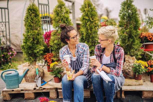 istock Two beautiful florists sitting palette, talking and drinking coffee. All around them plants and flowers. 1147992840