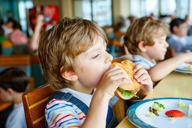 istock Cute healthy preschool boy eats hamburger sitting in school canteen 1147993767