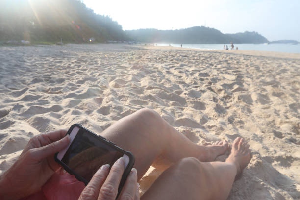 istock Woman uses phone while sitting on beach 1147997636