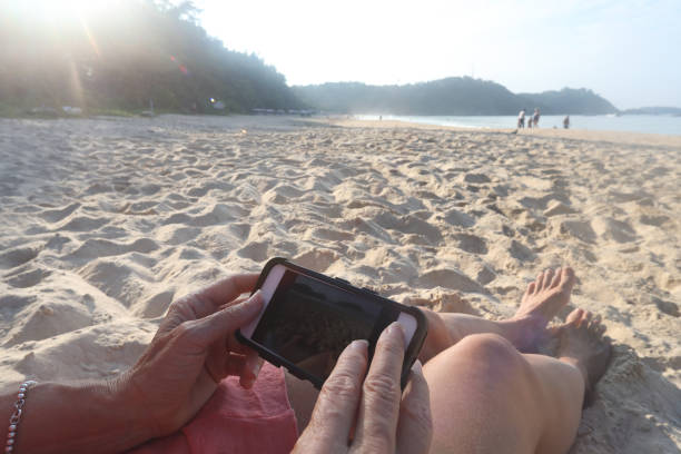 istock Woman uses phone while sitting on beach 1147997684