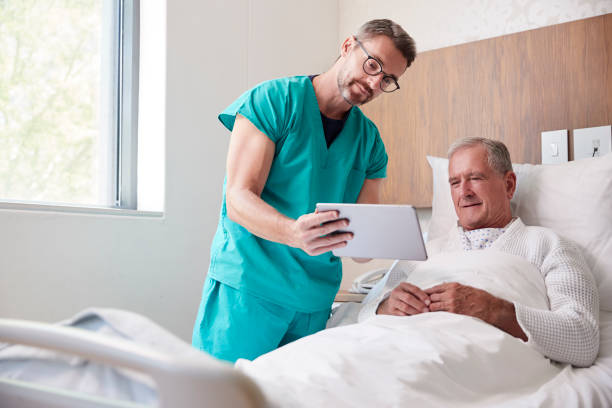 cirurgião com tabuleta de digitas que visita o paciente masculino sênior na cama de hospital na unidade geriátrica - hospital patient bed doctor - fotografias e filmes do acervo