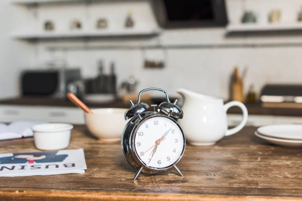 selective focus of vintage alarm clock at wooden table in kitchen