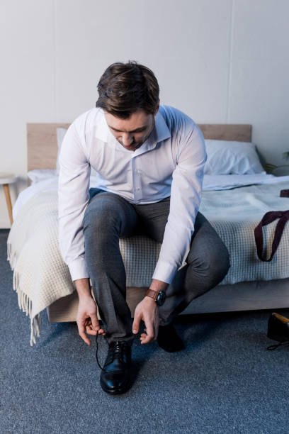 istock handsome man putting black shoes on, while sitting on bedding at home 1148004735