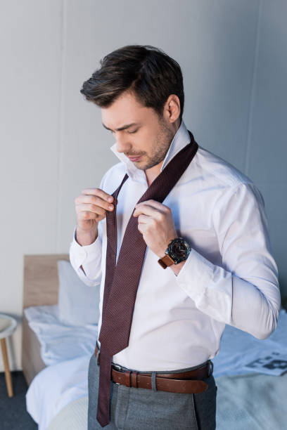 istock handsome confident man putting tie on while standing near bedding at home 1148004742