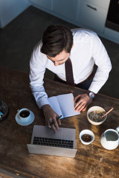 istock overhead view of man using laptop and writing in notebook while having breakfast at home 1148004801
