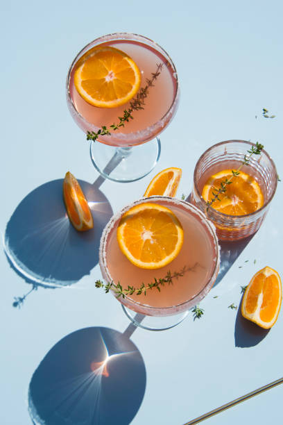 istock Grapefruit and thyme cocktails, refreshing drinks with ice on a light blue background. Summer garden party still life with orange and cold drinks, trendy retro style with artistic shadows. 1148005416
