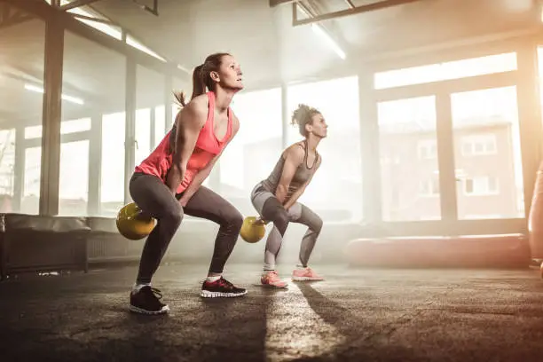 Two woman lifting kettle bell in gym gym