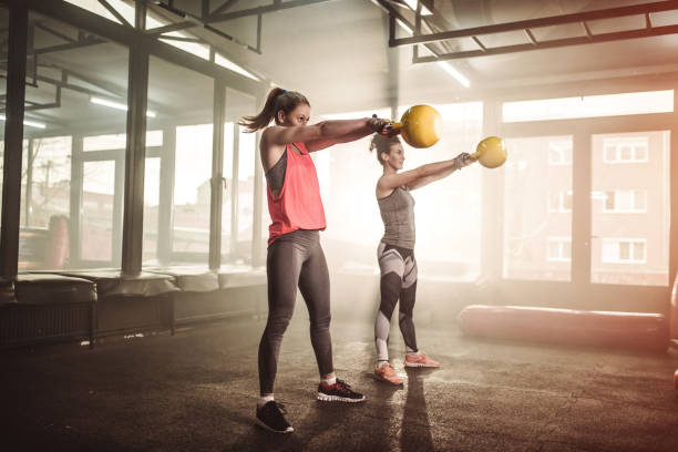 Two woman lifting kettle bell in gym gym stock photo
