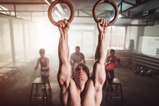 istock gym workout. Muscular build man on gymnastic rings. Synchronized unrecognizable people jumping on chairs. 1148008279