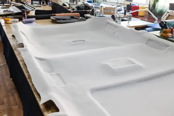 Gray ceiling lining removed from the car for tuning and bracing with grey soft material on a table in the workshop on the background of tools and equipment for working with the interior of vehicles