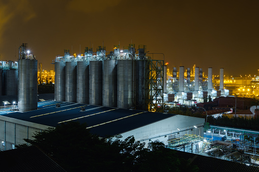 Glitter lighting of petrochemical industrial estate at night with storage silo in warehouses