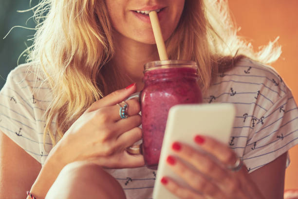 istock Beautiful woman using cellphone while drinking smoothie outdoors. 1148015333
