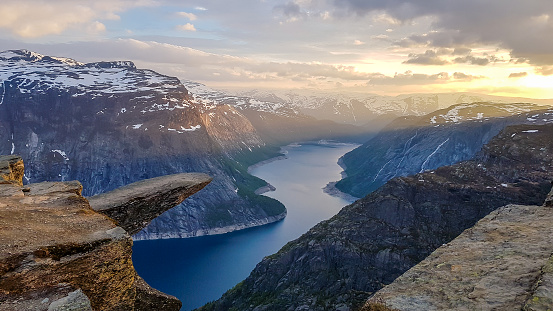 Famous rock formation, Trolltunga with a view from the above on Ringedalsvatnet lake, Norway. Rock hanging. Slopes of the mountains are partially covered with snow. Soft colors of the sunrise