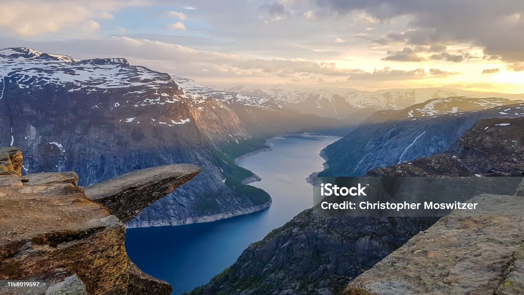 Norway - Famous Trolltunga during the sunrise with beautiful view on the fjord Famous rock formation, Trolltunga with a view from the above on Ringedalsvatnet lake, Norway. Rock hanging. Slopes of the mountains are partially covered with snow. Soft colors of the sunrise Norway Stock Photo