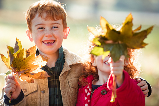 Portrait of two children in a public park holding leaves which they have collected.