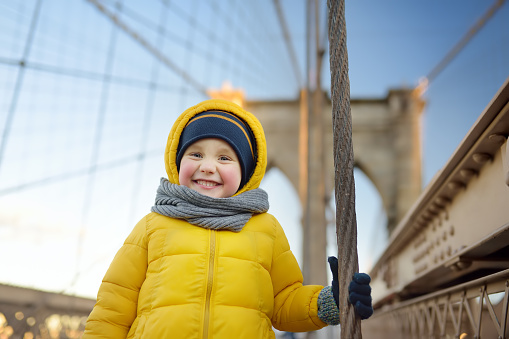 Cute little boy on Brooklyn Bridge with skyscrapers on background. Family travel with children.