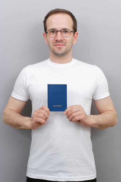 彼の手の中でパスポートを持つヨーロッパ人男性、メガネを着用し、白い t シャツ、パスポートを持つ国の市民、男とスタジオの写真 - travel vacations studio shot vertical ストックフォトと画像