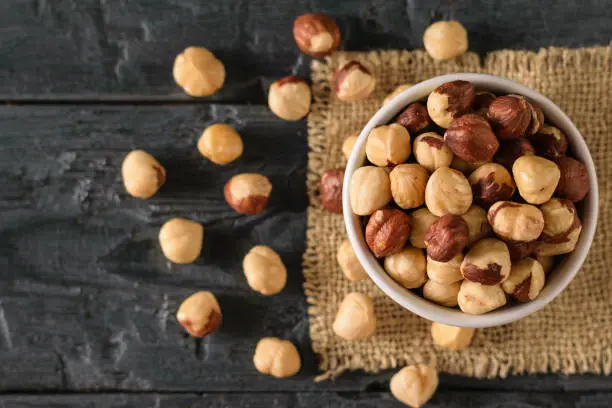 Scattered on the table roasted hazelnuts on a black wooden table. Prepared with the harvest of hazelnuts. The view from the top.