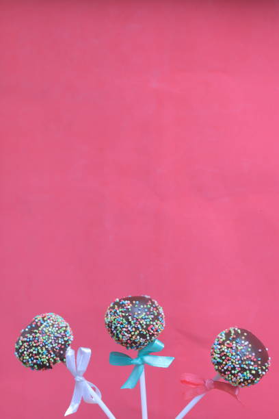 istock Cake Pops in chocolate with colored sprinkles. Decorated with a ribbon bow. On a red background 1148032142