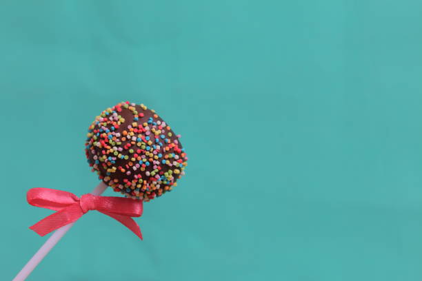 istock Cake Pops in chocolate with colored sprinkles. Decorated with a ribbon bow. On a mint background. 1148032193