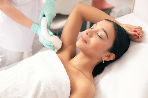 Smiling woman undergoing laser hair removal on her armpit Calm young woman lying with closed eyes and putting on arm up while having laser hair removal procedure on it hair removal photos stock pictures, royalty-free photos & images
