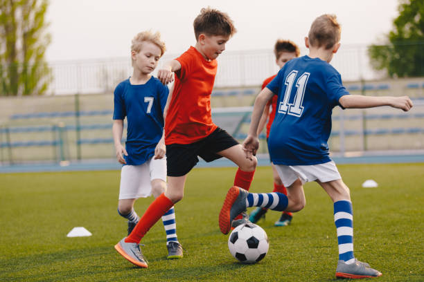 サッカー場でボールを蹴る若いサッカー選手。サッカー水平背景。青少年ジュニアアスリートの赤と青のサッカーシャツ - 子供サッカー ストックフォトと画像