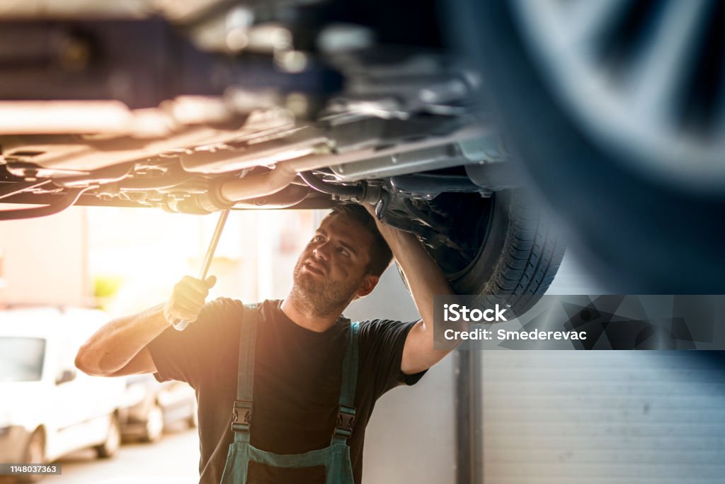 Car mechanics under the vehicle repairing automobile in his workshop. Car mechanic working. Auto Repair Shop Stock Photo