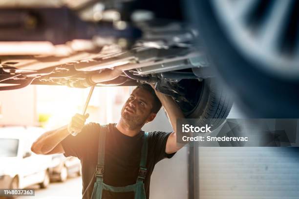 Car Mechanics Under The Vehicle Repairing Automobile In His Workshop Stock Photo - Download Image Now