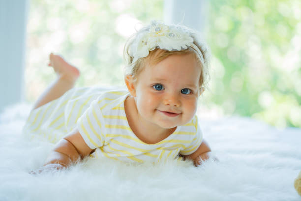 Cute nine months old baby girl lying on front on fluffy white blanket on bed.