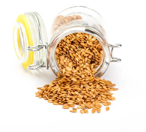 Golden flax seeds. Micronutrient beneficial for the organism that prevents and cures ailments. In glass jar on white background. Rich in fiber and nutrients (manganese, vitamin B1, and above all, in omega-3 fatty acids) beneficial for healt (skin, weight loss, cholesterol reduction, celiac, antioxidants,"u2026)