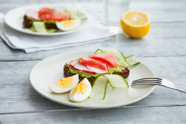 istock Two smorrebroad sandwiches with red fish,Avocado,eggs and cucumber on plate on a table 1148043607
