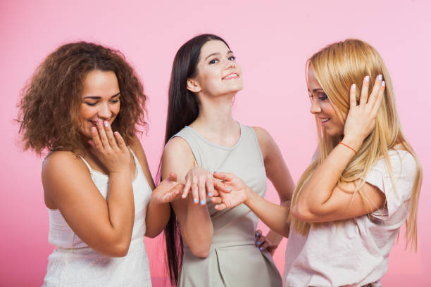 Girl show her female friendg her engagement ring Girl show her female friendg her engagement ring. Women admire new gold ring. Blonde curly brown and long dark hair. Pink background tres objetos stock pictures, royalty-free photos & images