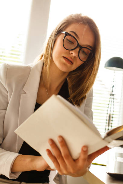 istock Young woman with eyeglasses reading a book 1148047506
