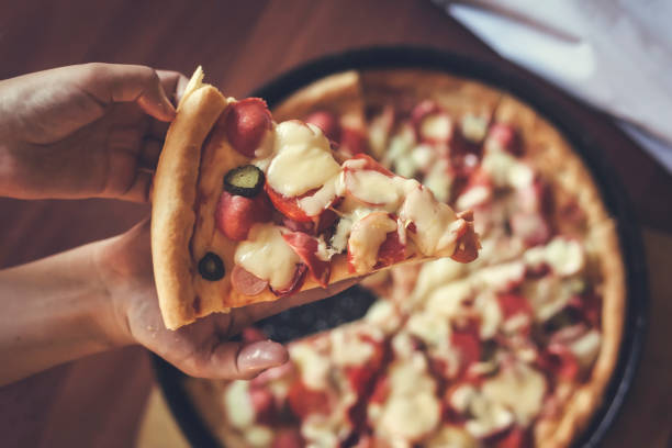 istock Person's hand holding a piece of pizza 1148048013