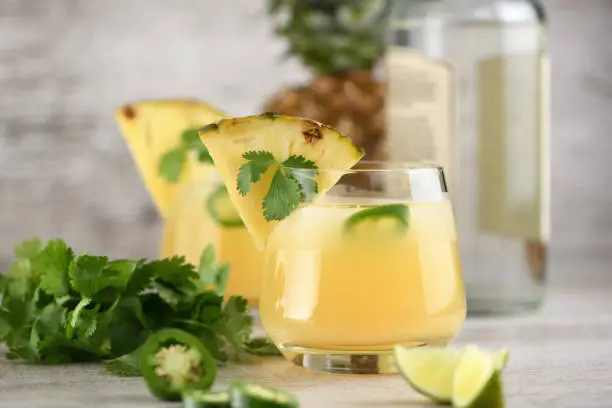 Tequila cocktail with pineapple juice, jalapeno  slices and cilantro, cooled with ice