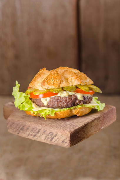 Juicy fresh burger with onions, fresh roasted meat with beef, pork, pickled cucumbers and gherkins, sauce, tomato lies on a vintage old rustic board, black kitchen stone slate, flies and leaves, remov jugosa hamburguesa fresca con cebollas, carne asada fresca con carne de res, cerdo, pepinos en escabeche y pepinillos, salsa, tomate se encuentra en una antigua tabla rústica vintage, pizarra de piedra de la cocina negra, moscas y hojas, remov