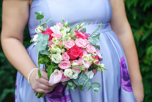 Close-up shot of Caucasian female guest or bridesmaid wearing a lilac summer dress which shows a lovely baby bump and holding a delicate free-form bouquet featuring different color roses, pink callas and greenery.