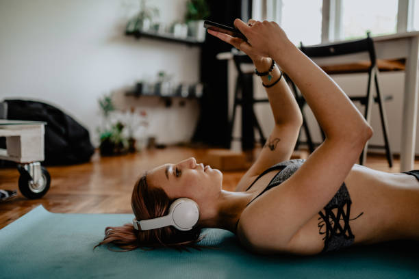 mujer haciendo yoga y usando teléfono inteligente en casa - stretching yoga zen like beauty fotografías e imágenes de stock