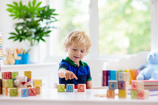 Child learning letters and numbers. Kid with colorful wooden abc blocks. Little boy spelling words with educational block toys. Kids doing school homework at white desk. Bedroom for preschool children
