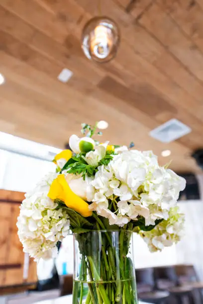 Closeup vertical view of wedding flower bouquet arrangement on table of reception dinner in restaurant venue with ceiling in rustic restaurant