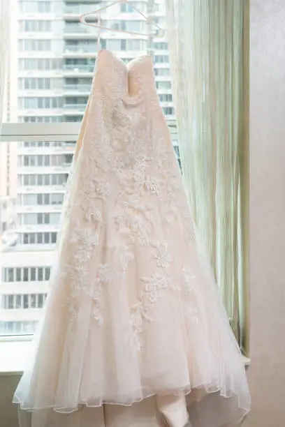 Long wedding dress hanging on hanger of window windowsill in urban modern New York City NY NYC hotel high rise apartment condo building