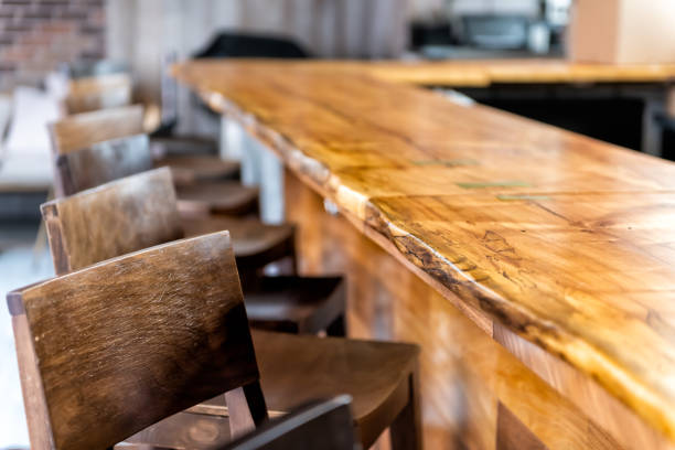 row of empty wooden vintage bar stools by counter in drink establishment pub during day closeup of retro wood and nobody - business styles foods and drinks drinking imagens e fotografias de stock