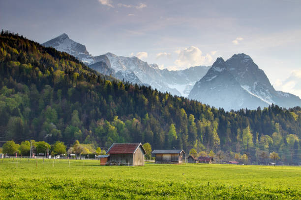 pequeños graneros de heno de madera y casas en el prado soleado bajo el cielo azul con puntiagudo alpspitze waxenstein zugspitze picos en la nieve, wetterstein norte de piedra caliza alpes garmisch partenkirchen bayern alemania europa - waxenstein fotografías e imágenes de stock