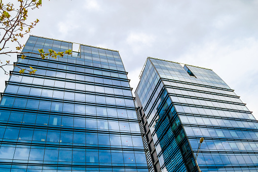 Twin skyscrapers with glass windows on a stormy day with clouds reflecting blue on the exterior of the buildings. Economy, business concept.