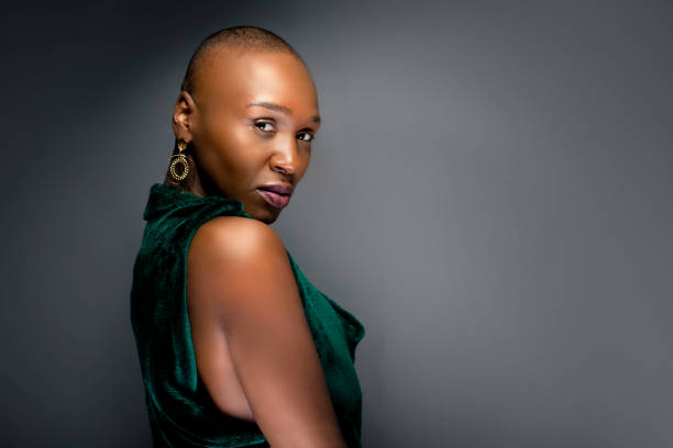 Black African American female fashion model with a bald hairstyle in a studio.  The portrait shows the beauty and confidence of the bold and trendy glamour hairdo style.
