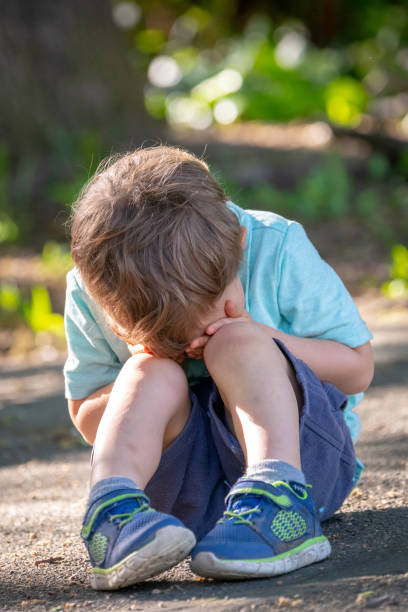 niño llorando sentado en el suelo cubriendo su cara - displeased child abandoned child abuse fotografías e imágenes de stock