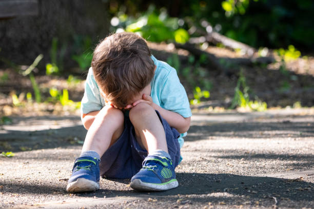 Crying toddler sitting on the floor covering his face stock photo