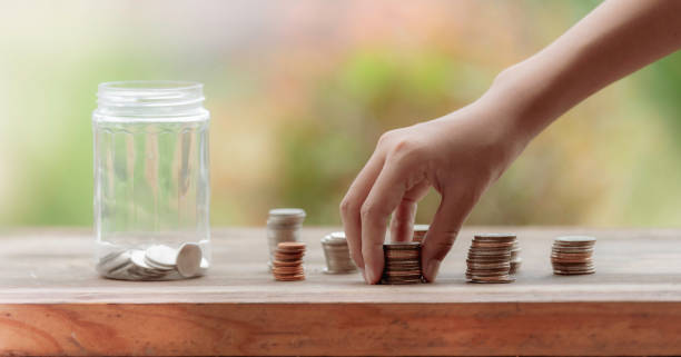 Closeup for hand Little girl picking up pile coin for saving money into piggy bank for future life. Investment and Saving Concept. stock photo
